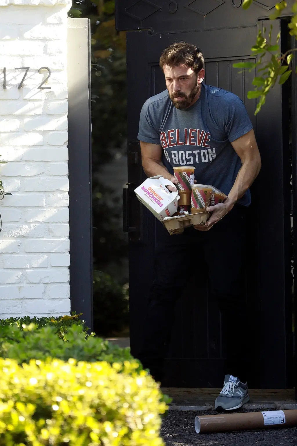 Ben Affleck carrying Dunkin' coffee and Munchkins out a doorway.